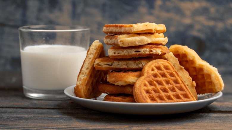 white plate of heart-shaped waffles next to a glass of milk