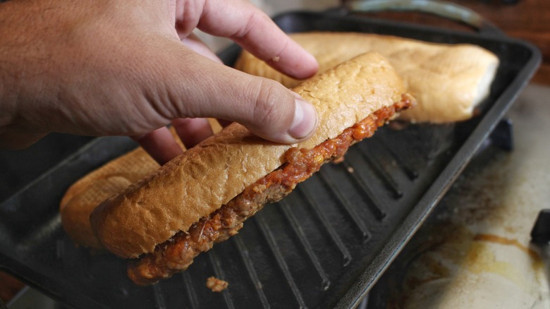 hand holding chorizo sandwich over grill