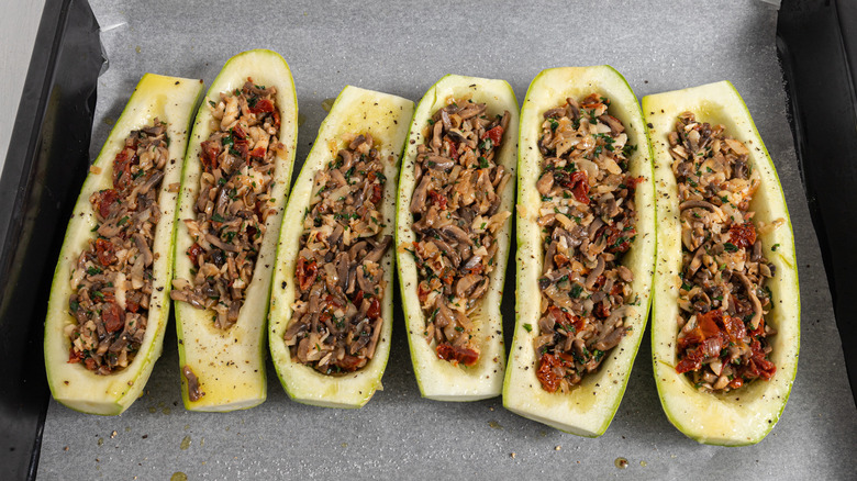 Zucchini boats filled with mushroom filling on a parchment paper-lined baking tray.