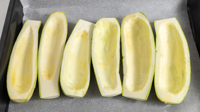 Six zucchini halves on a parchment paper-lined baking tray.