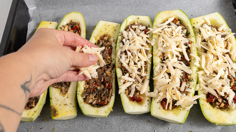 Sprinkling shredded cheese over zucchini boats.