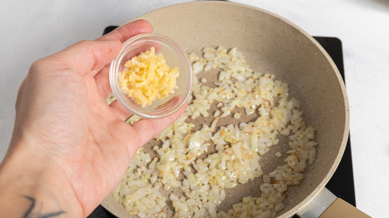 Minced garlic being added to a pan with chopped onion.