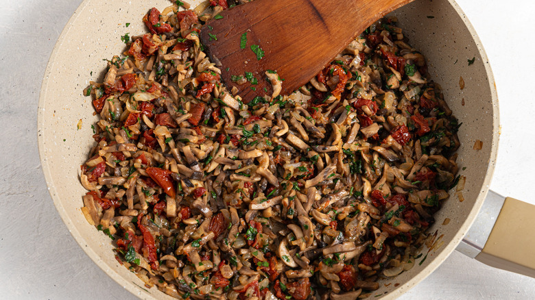 A skillet with cooked filling for mushroom zucchini boats.