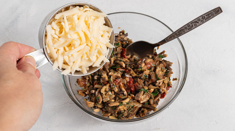 Filling for mushroom zucchini boats in a bowl with shredded cheese added to it.