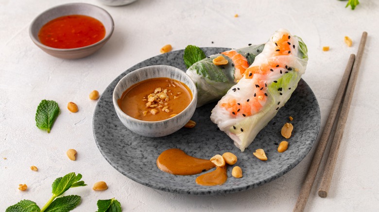 Summer rolls with peanut sauce on a plate with loose peanuts and mint leaves