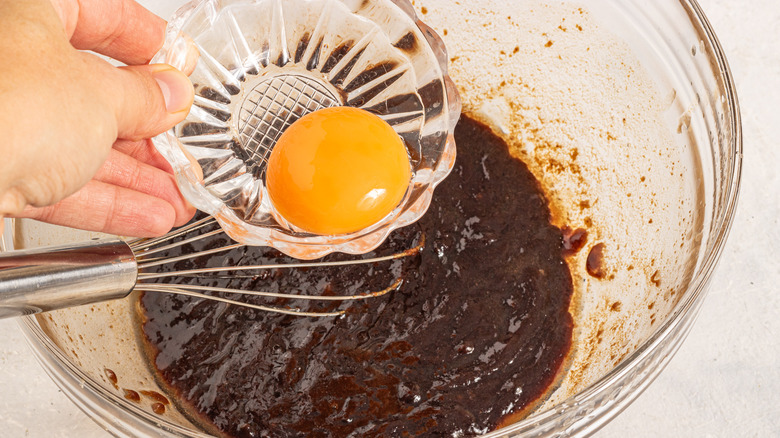 Adding egg yolk to a bowl with dark brown sugar and melted butter mixture