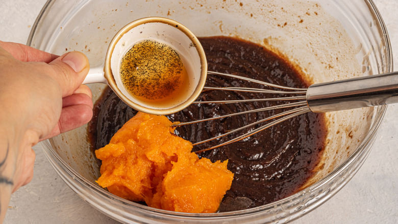 Adding vanilla extract to a bowl with pumpkin puree and dark brown sugar mixture