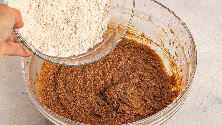 Adding flour to a bowl with brown batter