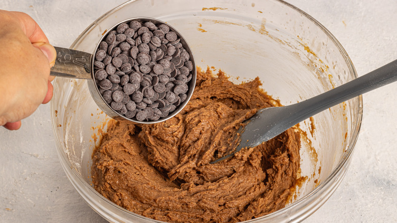 Adding chocolate chips to a bowl with brown batter