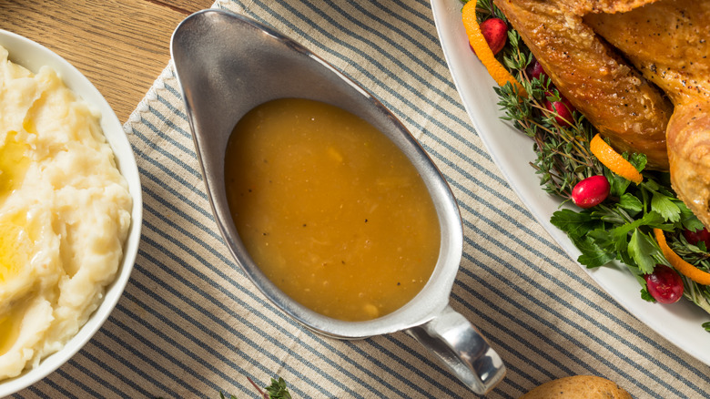 gravy boat with turkey gravy in between a platter with turkey and a bowl of mashed potatoes