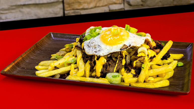 A tray full of chorrillana topped with leeks on a red table