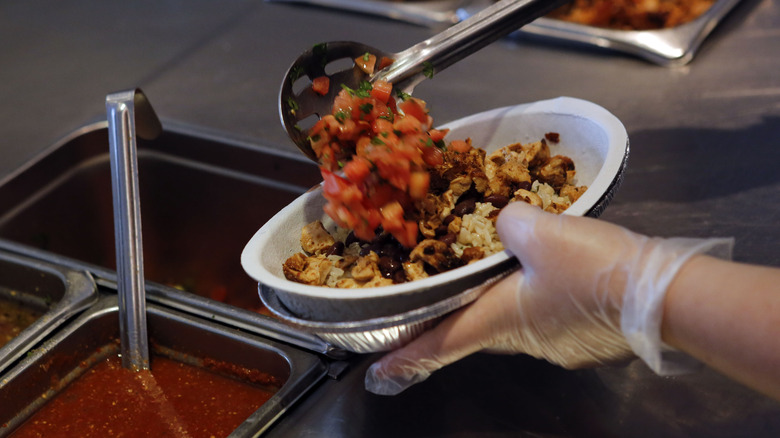 Employee scooping pico de gallo into chipotle bowl