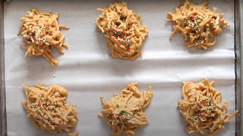 Peanut butter haystack cookies sit on a baking sheet and are topped with festive sprinkles