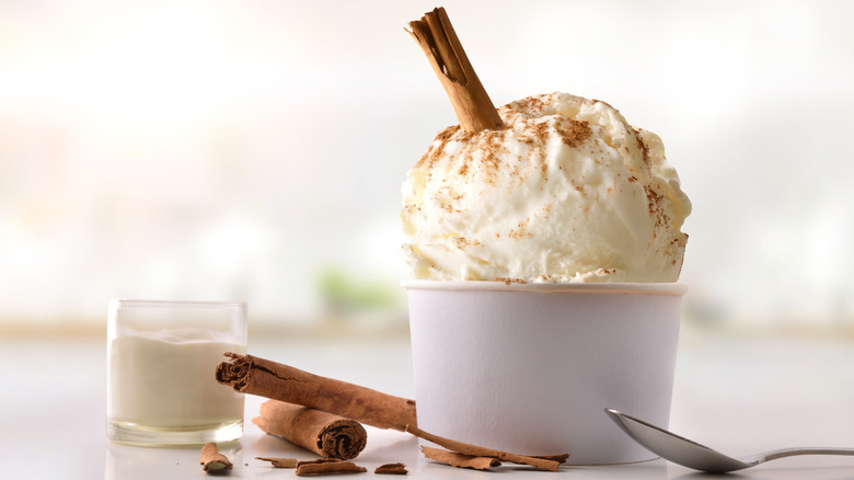 A scoop of ice cream with a cinnamon stick poking out on a table with more cinnamon sticks