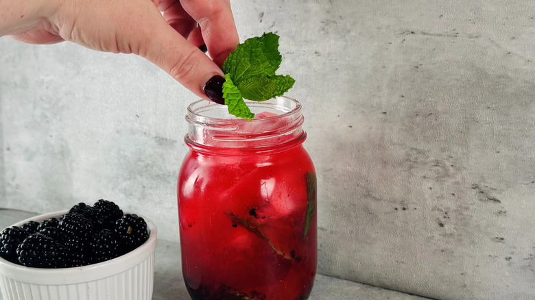 Hand placing mint onto blackberry mojito in jar