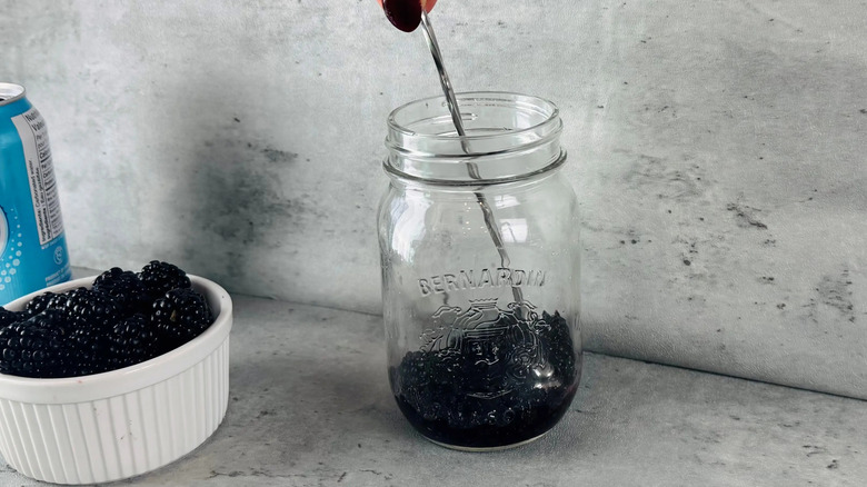 Spoon crushing blackberries in glass jar