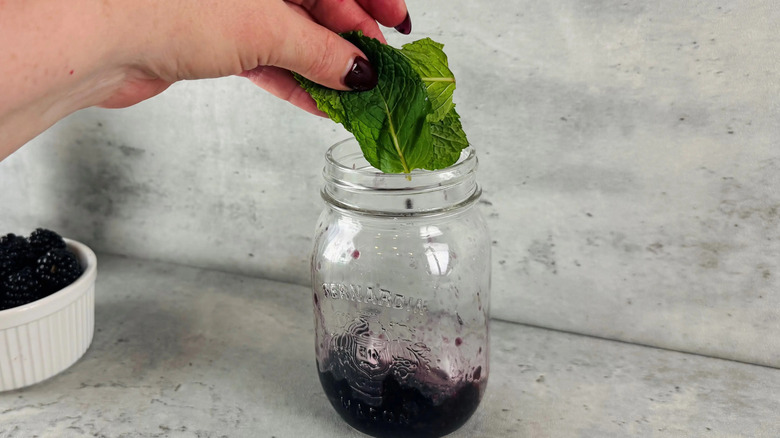 Hand adding fresh mint leaves to glass jar