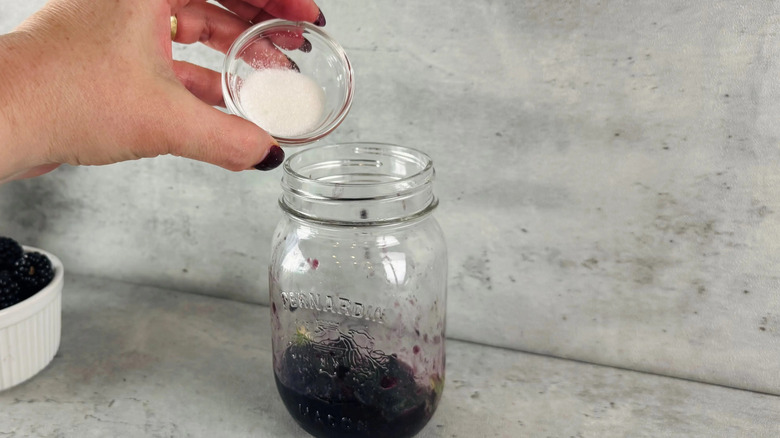 Hand pouring white sugar into glass jar