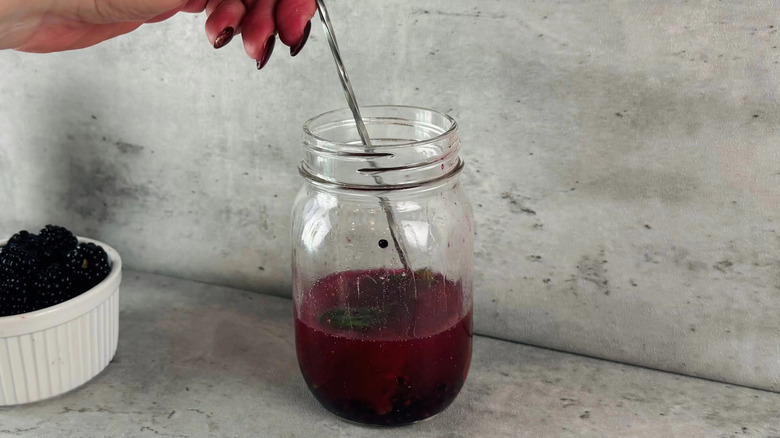 Hand stirring blackberry cocktail in glass jar