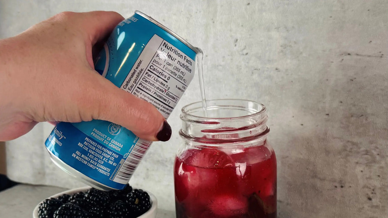 Can of club soda pouring into glass jar