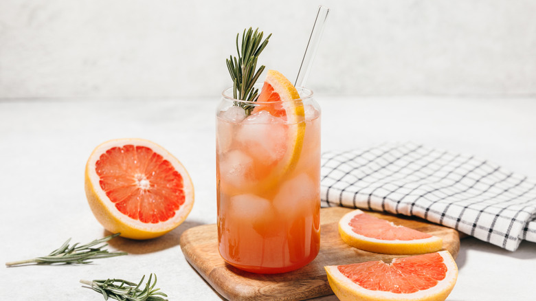 A grapefruit juice and tequila cocktail with a sprig of rosemary in a tall cocktail glass