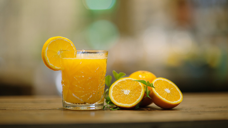 A glass of orange juice sits on a wooden table next to slices of oranges