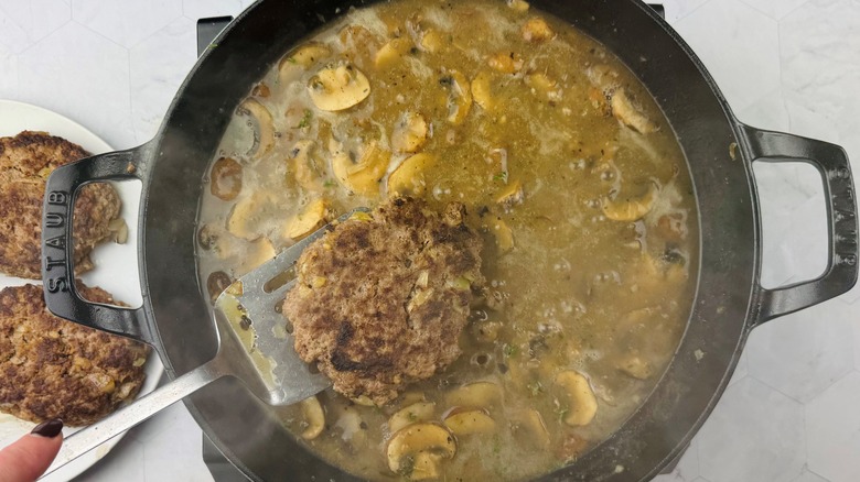 placing beef patty in skillet with mushroom gravy