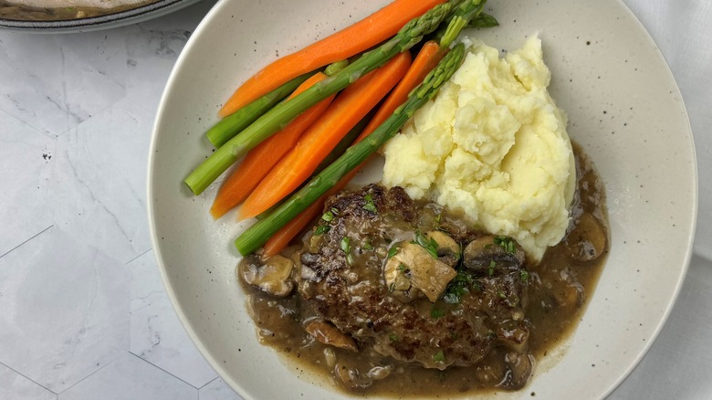 portion of salisbury steak with mushroom gravy, mashed potatoes, carrots, and asparagus