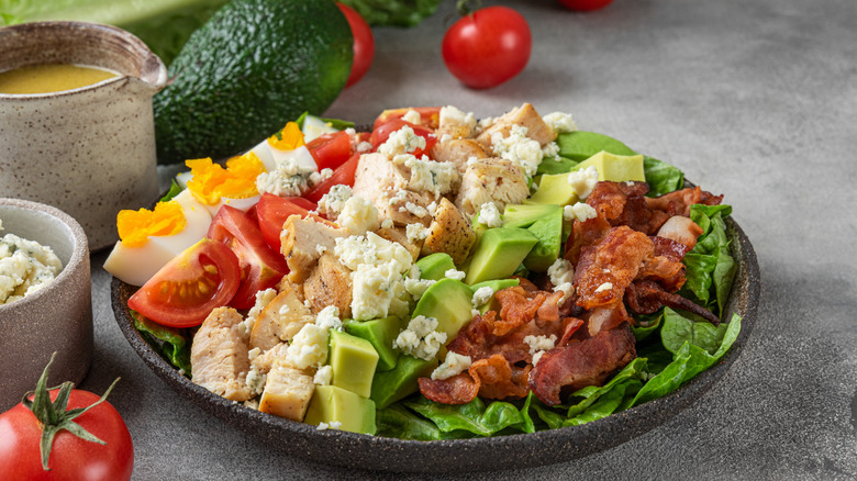 Cobb salad with rows of ingredients in a stone bowl next to a bowl of dressing and blue cheese