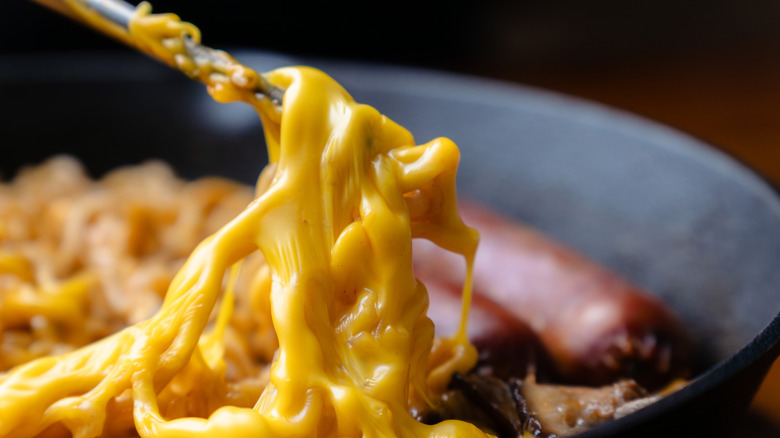 A metal utensil lifts some cheesy ramen from a dish