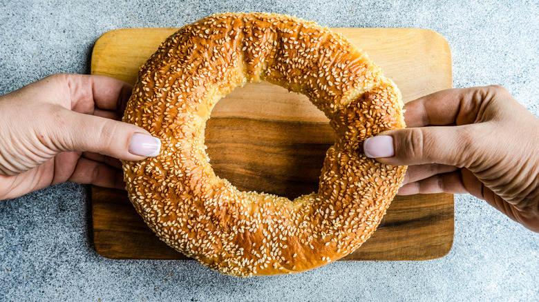 Hands holding a sesame bagel over cutting board