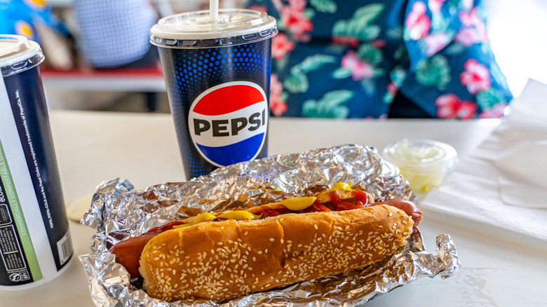 A Costco hot dog wrapped in tin foil and Pepsi soft drink sit on a Costco food court table