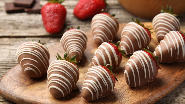 Chocolate covered strawberries with a white chocolate drizzle sit on a wooden tray