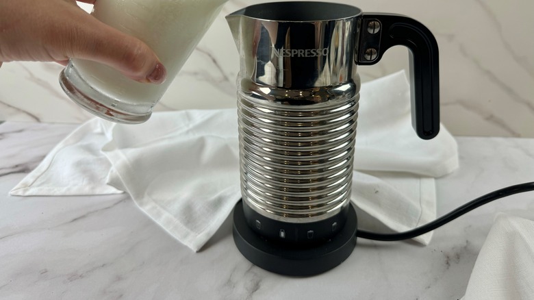 hand pouring milk in frother