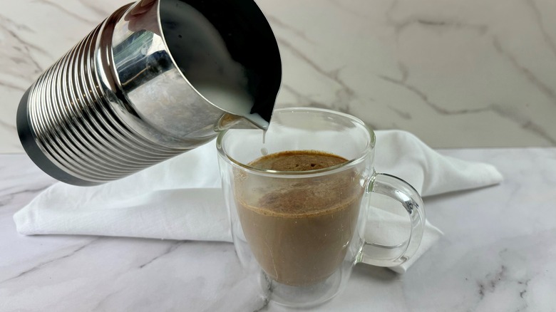 hand pouring milk into coffee