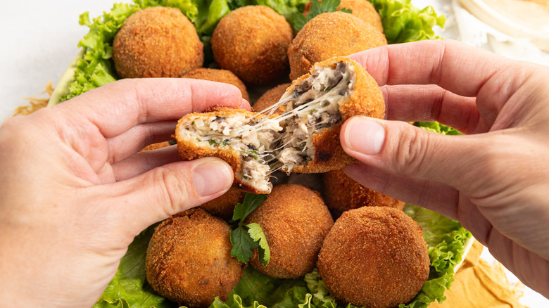 Hands pulling cheesy croquette apart