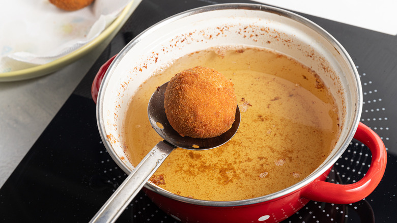 slotted spoon holding croquette over oil