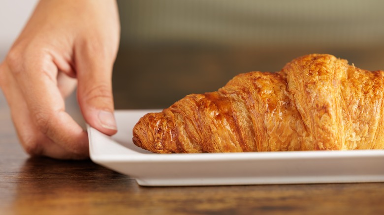 Hand grasping croissant on a white plate