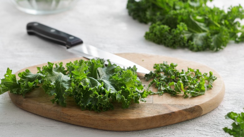 Chopped curly kale on a wooden board with a knife on side