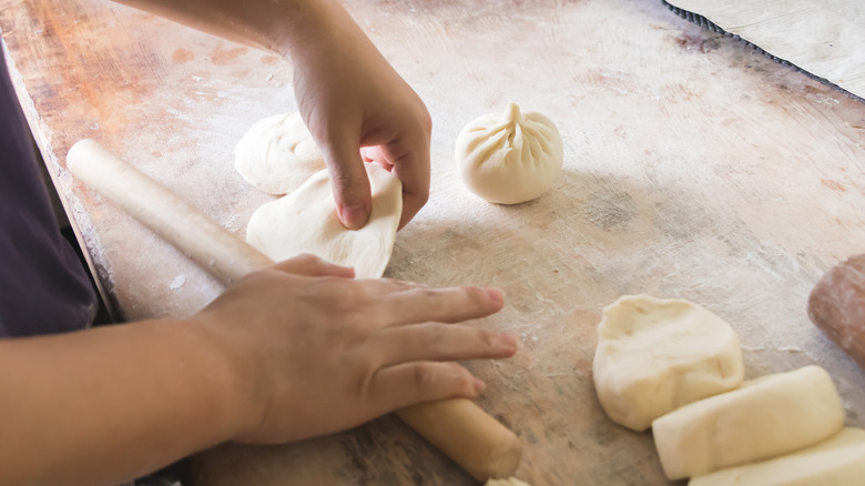 person shaping closed bao buns on floured countertop