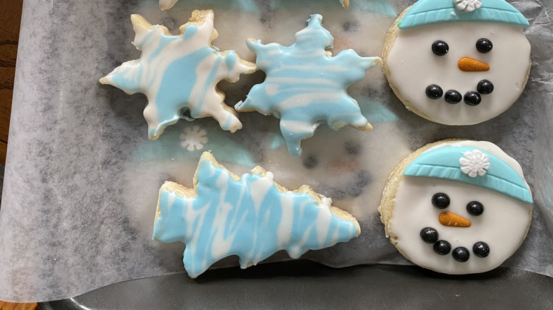 Cookies with marble royal icing and other snowman decor on a baking tray with parchment paper