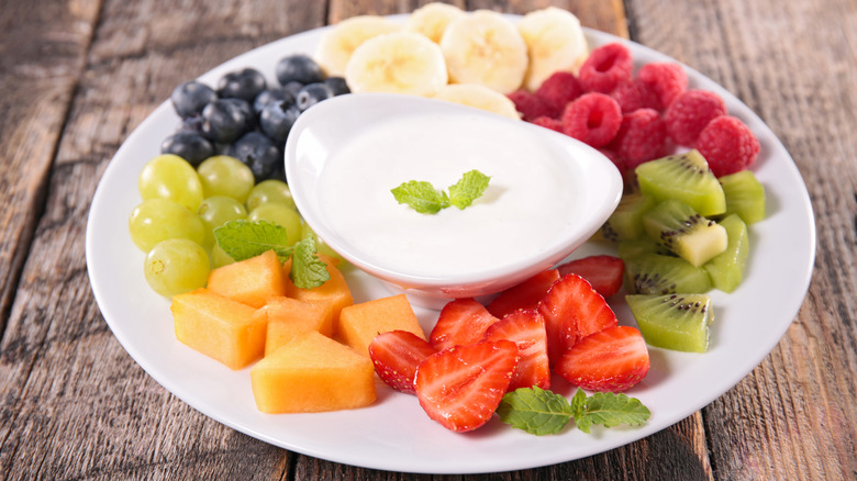 Various fruits are displayed with white fruit dip in the center of a plate.