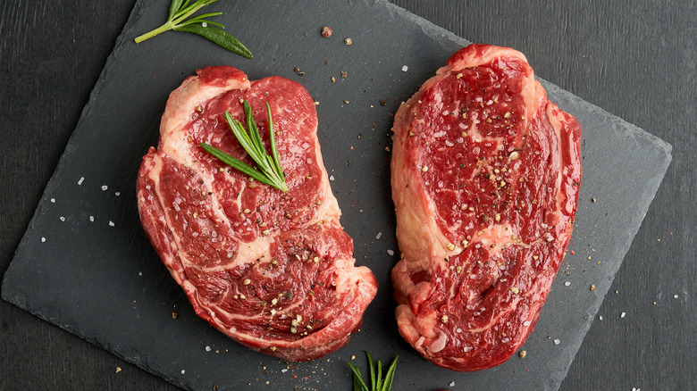 Thick raw ribeye steaks on a board