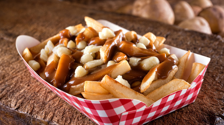 Poutine in a red and white to go container on a hard wood surface