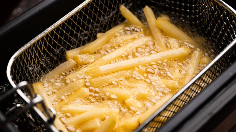 A serving of french fries sit in a fryer filled ith hot, boiling oil