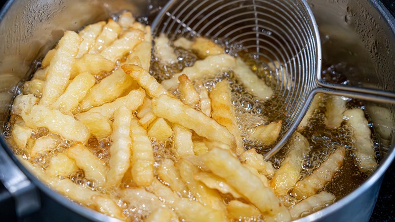 Crinkle french fries frying in pot with metal strainer inside