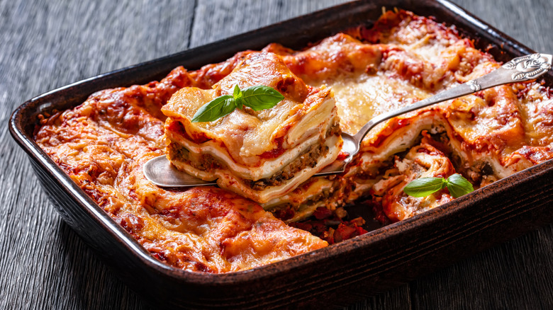 A silver spatula digging out a piece of lasagna from baking pan