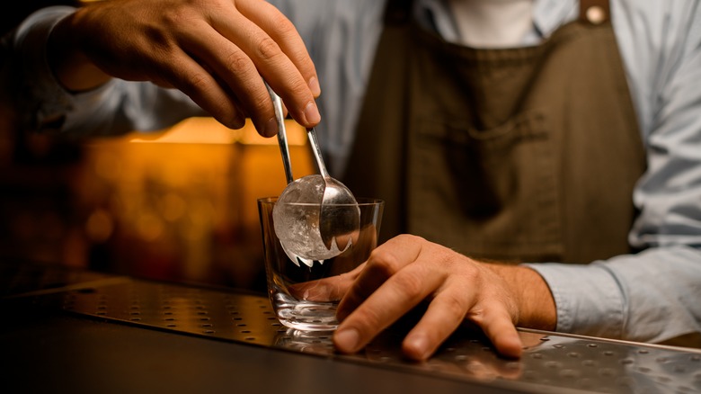 bartender using ice tongs to fill cocktail glass