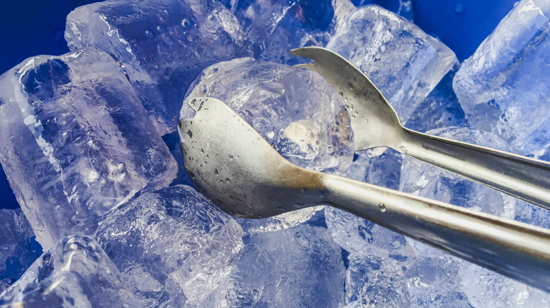 Ice tongs grabbing ice in a blue bucket