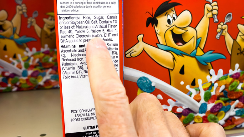 A finger hovers over the ingredient label on a box of Fruity Pebbles cereal